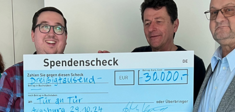 Mitglieder des Tür an Tür-Vorstands und Vertreter der Hans und Anna Adlhoch-Stiftung präsentieren gemeinsam einen großen Spendenscheck in Höhe von 30.000 Euro vor dem WohnProjektHaus.