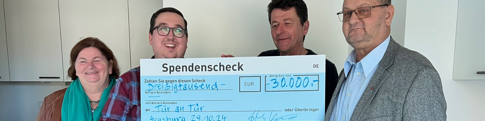 Mitglieder des Tür an Tür-Vorstands und Vertreter der Hans und Anna Adlhoch-Stiftung präsentieren gemeinsam einen großen Spendenscheck in Höhe von 30.000 Euro vor dem WohnProjektHaus.