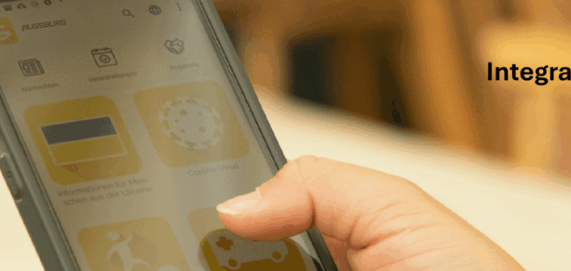 Hand hält Smartphone mit geöffneter Integreat-App – Symbol für digitale Hilfe bei Tür an Tür in Augsburg.