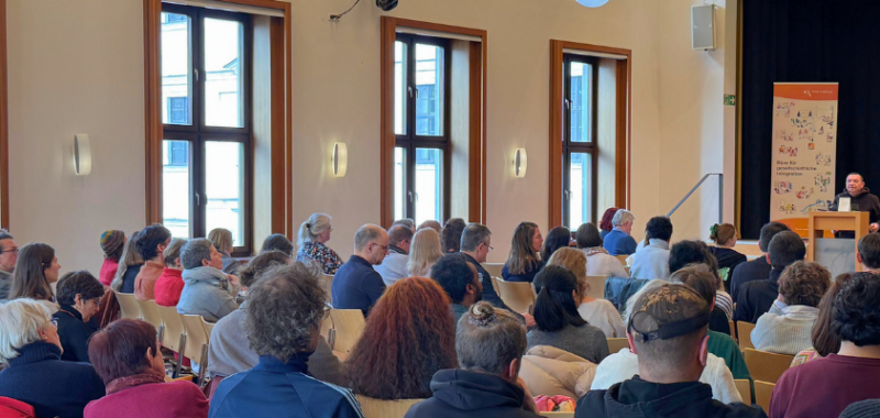 Publikum beim Runden Tisch „Vielfalt im Fokus“ in Augsburg, am Rednerpult wird über Integration und Migration geredet.